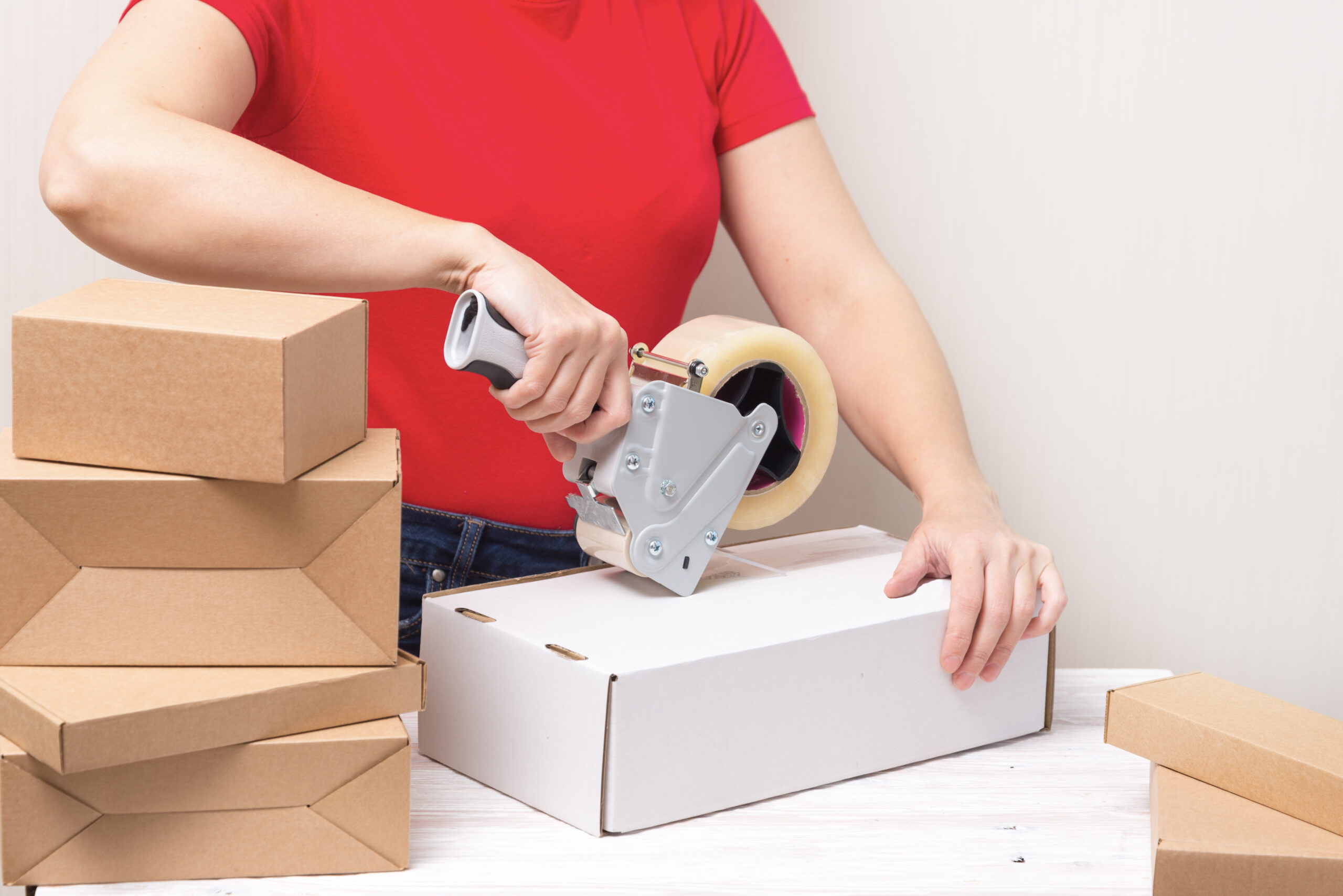 Woman packing cardboard boxes using tape dispenser